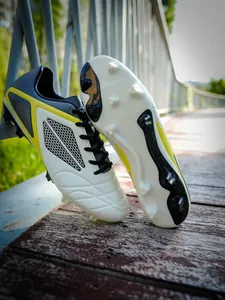Professional soccer cleats with white leather and yellow accents showing FG stud outsole.