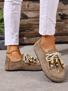 Detail von braunen Wildleder-Loafers mit bunten Perlen an Schnürsenkeln und weißer Hose.