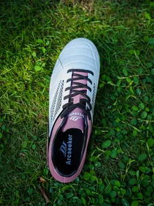 Close-up top view of Arcseeker professional white and pink soccer shoe on green grass