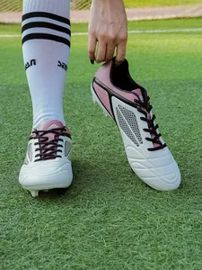 Detailed macro view of professional pink and white soccer cleats on a green grass field