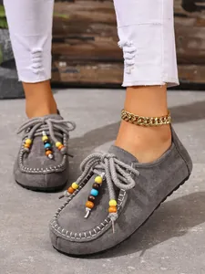 Nahaufnahme grauer Wildleder-Slipper mit bunten Perlen und weißen Kontrastnähten