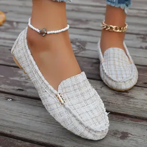 Detailed view of stylish white tweed loafers with gold buckle on a rustic wooden background