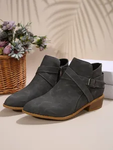 Close-up of grey pointed-toe Chelsea boots with cross straps and side zipper detail.
