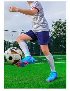 Actiefoto van blauwe en roze voetbalschoenen op een kunstgrasveld tijdens training.