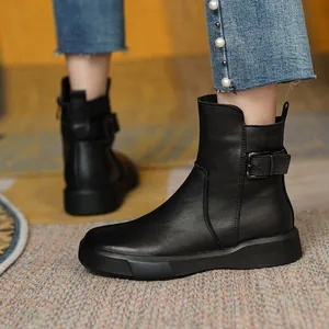 Side view of black flat leather ankle boots with decorative buckle strap on a textured rug.