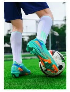 Detailweergave van turkooizen gebreide voetbalschoenen met oranje FG-noppen op gras