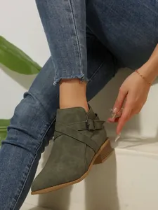 Detail view of olive green pointed-toe ankle boots with buckle strap and block heel.