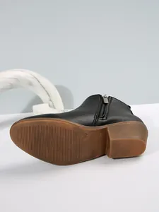 Detail van zwarte enkellaars met blokhak, zool met textuur en rits aan de zijkant