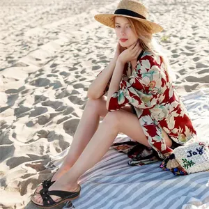 Lifestyle view of black floral wedge platform sandals worn by a model on a sunny beach