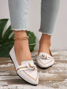 Detail shot of white fly-knit pointed flats with decorative bow and gold trim.