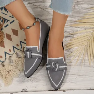 Détail de chaussures plates grises à bout pointu avec nœud décoratif sur sol en bois