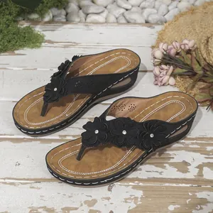 Primer plano de chanclas de cuña negras para mujer con tres flores decorativas y pedrería