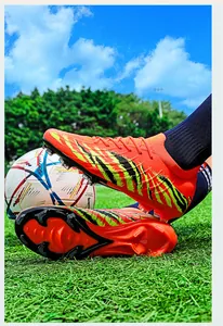 Vue détaillée de chaussures de football en tricot orange avec crampons AG sur herbe verte