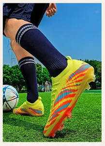 Vue détaillée des chaussures de football jaunes Fly-Knit avec rayures oranges sur gazon