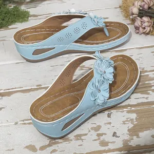 Detalle de chanclas con cuña azul claro y flores sobre un fondo de madera rústica.
