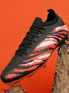 Chaussure de foot noire à rayures tigrées rouges sur socle en bois naturel