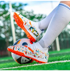 Detail of white flyknit soccer shoes with colorful patterns and orange turf soles on grass
