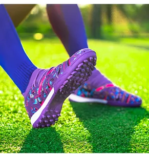 Close-up of purple knitted football boots showing TF turf sole on green grass field.