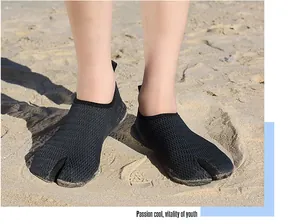 Detailed view of black mesh split-toe water shoes worn on a sandy beach