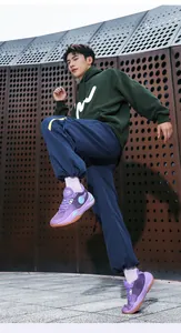 Dynamic lifestyle shot of purple low-top basketball shoes on an Asian male model outdoors