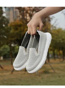 Handheld close-up view of light grey breathable fly-knit mesh slip-on walking shoes for outdoors