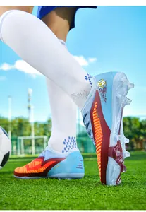Close-up detail of blue and red fly-knit soccer shoes with FG cleats on grass field