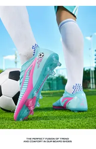 Cyan and pink knitted soccer shoes with FG/HG long studs on green grass field