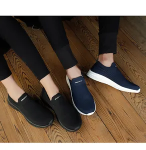 Close-up of black and navy blue breathable fly-knit slip-on sneakers on a wooden floor.