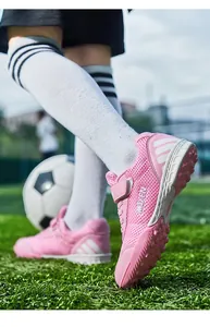 Chaussures de football roses pour enfants avec bande velcro sur un terrain de sport