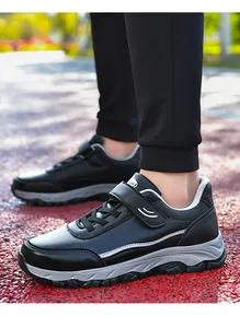 Close-up of black leather walking shoes with velcro straps in an outdoor park setting.