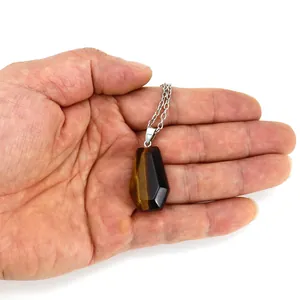Close-up of a tiger eye stone coffin pendant necklace held in a hand for scale reference