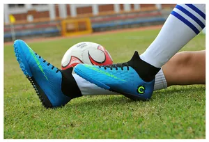 Close-up of blue high-top soccer shoes worn on a grass field with a ball nearby.