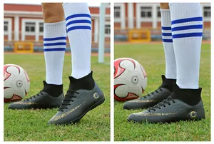 Detail view of black high-top soccer shoes with golden pattern on a grass football field.