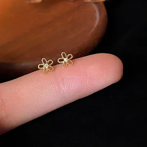 Detailansicht von mini 14K vergoldeten Blumenohrringen mit Zirkonia-Mitte auf Finger
