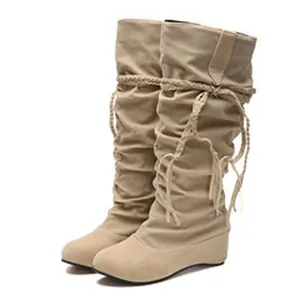 Close-up view of beige slouchy mid-calf boots with wedge heels and braided ropes.