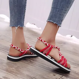 Primer plano de sandalias planas de cuerda trenzada roja y blanca usadas en suelo de madera