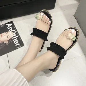 Detailed view of flat black slide sandals with ruffled straps and pineapple toe accent.