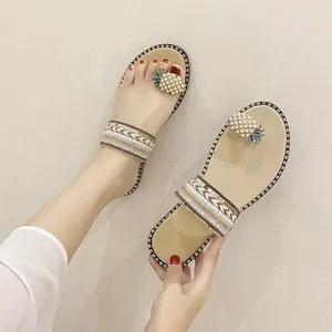 Detail view of flat toe-loop sandals with beaded pineapple embellishment and woven straps