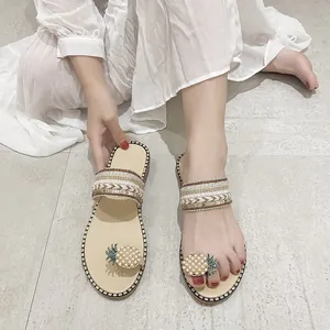 Detailed macro view of women's flat toe-ring sandals with pearl-studded pineapple charm.