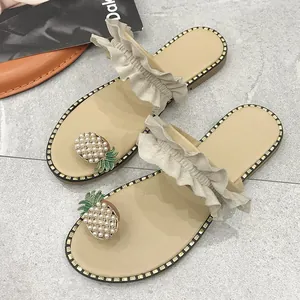 Detailed view of flat toe-loop sandals with ruffled straps and pearl pineapple decor.