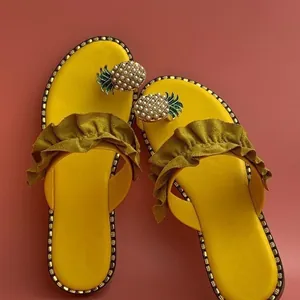 Overhead shot of vibrant yellow flat sandals featuring a faux pearl pineapple and ruffle strap