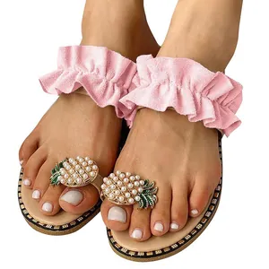Detail view of pink ruffled flat sandals featuring a pearl pineapple toe ornament.