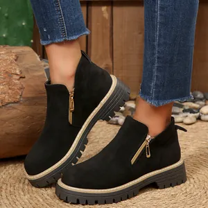 Gros plan de bottines noires en suédine avec fermetures éclair dorées et semelles épaisses
