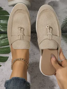 Gros plan de mules fermées en daim beige avec détails de boucles dorées élégantes