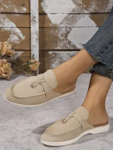 Détail de mules élégantes en daim beige avec boucle decorative portées par un mannequin