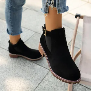 Close-up detail view of black suede ankle boots with buckle strap and square heel on feet.