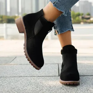 Close-up of black suede women's ankle boots with block heel and buckle strap outdoors