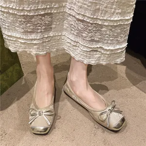 Close-up of retro ballet flats featuring metallic bow detail and contrasting toe cap