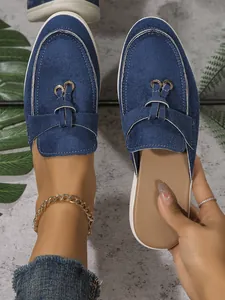 Vue de dessus de mules en daim bleu portées au pied et tenues à la main montrant la semelle