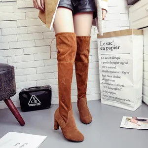Close-up of stylish brown suede over-the-knee boots with chunky high heels on model.
